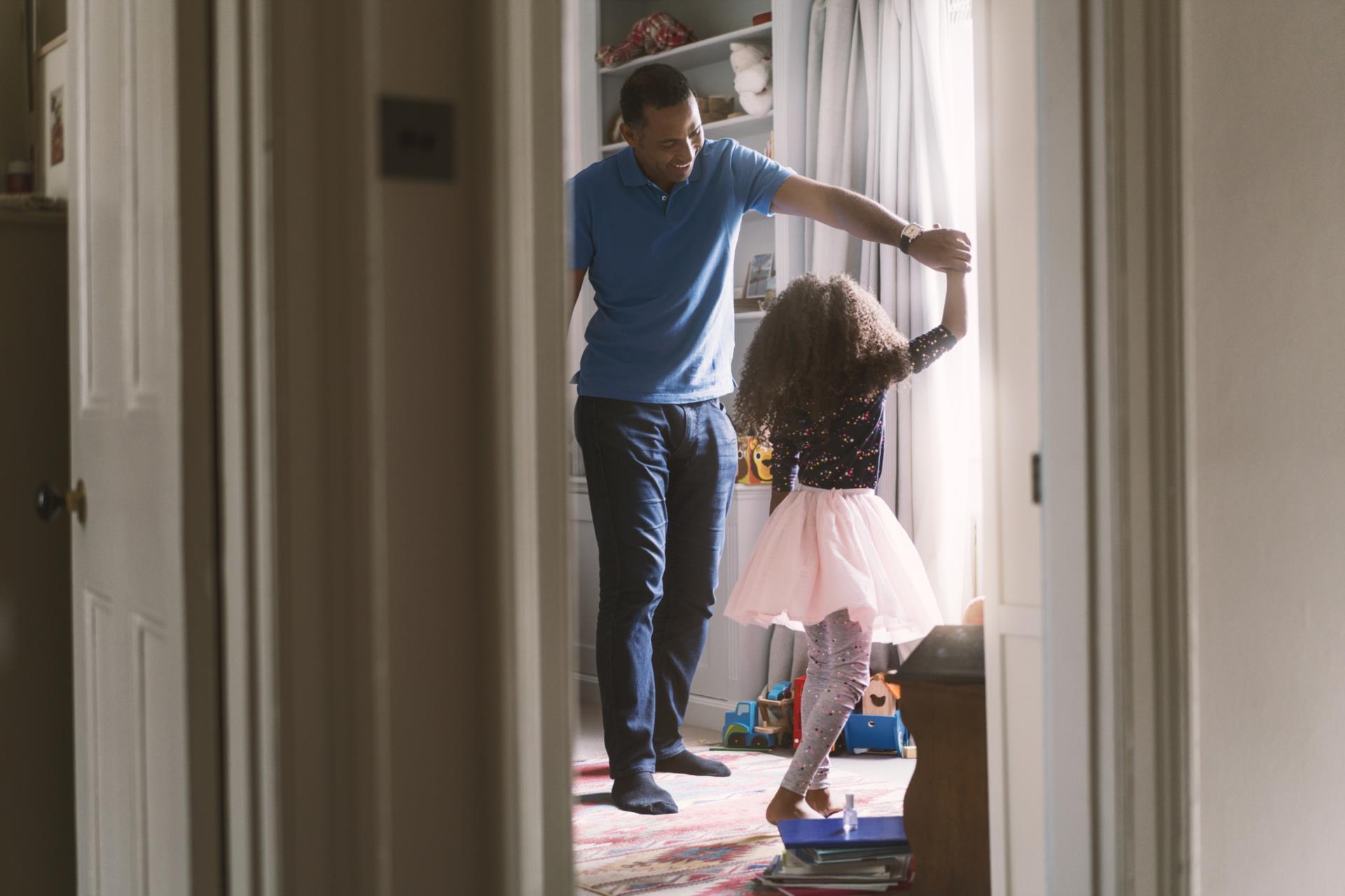A caregiver and older child wearing a tutu dancing at home.